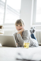 Smiling woman lying on the floor using laptop - JOSF01999