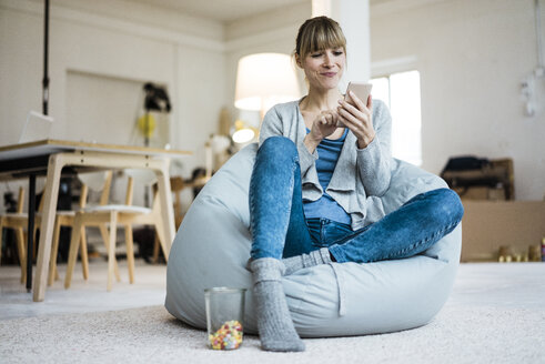 Smiling woman sitting in beanbag using cell phone - JOSF02002