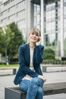 Smiling businesswoman sitting on bench talking on cell phone outdoors - JOSF02007