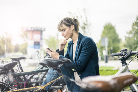 Businesswoman using cell phone outdoors surrounded by bicycles stock photo