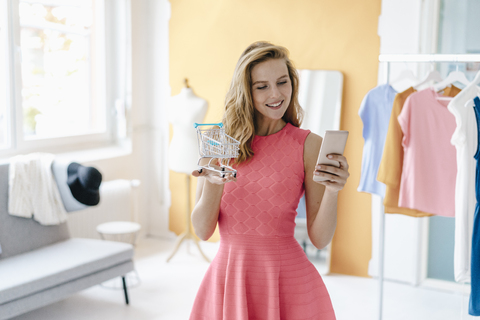 Lächelnde junge Frau im Modestudio, die ein Handyfoto von einem Einkaufswagenmodell macht, lizenzfreies Stockfoto