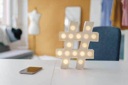 Beleuchtetes Hashtag-Schild auf einem Tisch in einem Modeatelier - KNSF02991
