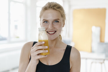 Porträt einer lächelnden jungen Frau in Sportkleidung, die einen Smoothie trinkt - KNSF03007