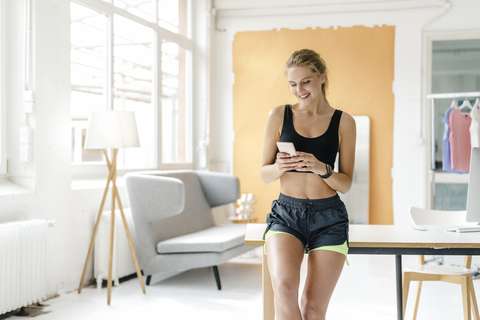 Lächelnde junge Frau in Sportkleidung schaut auf ihr Handy, lizenzfreies Stockfoto