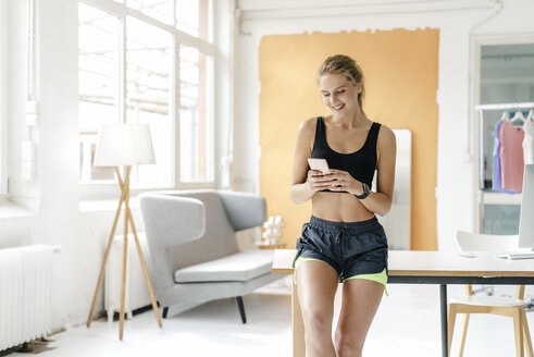 Smiling young woman in sportswear looking at cell phone - KNSF03013