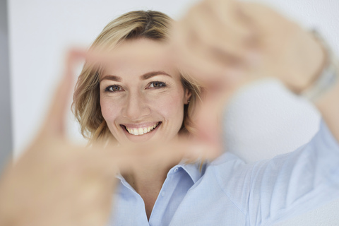 Porträt einer lächelnden blonden Frau, die mit ihren Fingern einen Rahmen baut und den Betrachter ansieht, lizenzfreies Stockfoto