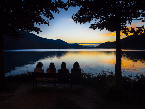 Österreich, Oberösterreich, Salzkammergut, Fuschlsee, Menschen sitzen auf einer Bank und genießen den Sonnenuntergang, lizenzfreies Stockfoto