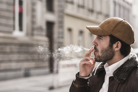 Porträt eines jungen Mannes mit Baseballmütze, der eine Zigarette raucht, lizenzfreies Stockfoto