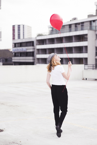 Rückenansicht einer jungen Frau mit rotem Luftballon, lizenzfreies Stockfoto