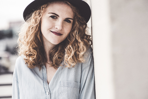 Portrait of smiling young woman wearing hat leaning against wall stock photo