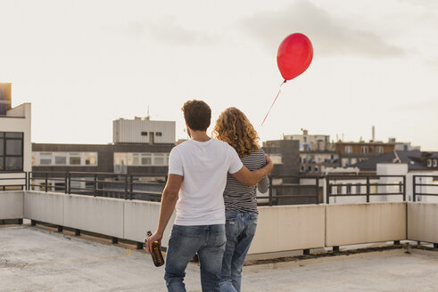 Back view of young couple on roof terrace at evening twilight - UUF12339