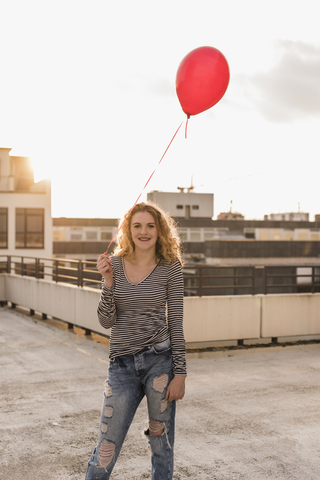 Portrait of young woman with red balloon on roof terrace at sunset stock photo