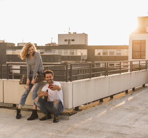 Young couple relaxing on roof terrace at sunset taking selfie with cell phone stock photo