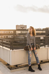 Junge Frau mit Skateboard genießt den Sonnenuntergang auf der Dachterrasse - UUF12354