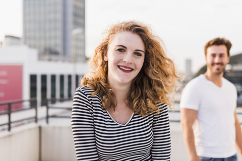 Portrait of happy young woman with boyfriend in the background at sunset stock photo