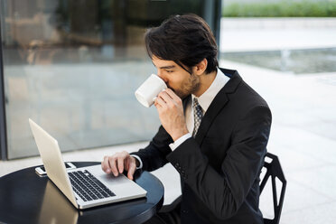 Businessman working on laptop and drinking coffee outdoors - VABF01379