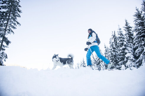 Österreich, Altenmarkt-Zauchensee, junge Frau mit Hund im Winterwald - HHF05537