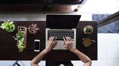 Draufsicht auf eine Frau, die einen Laptop mit Mobiltelefon und Pflanzen auf einem Holztisch benutzt, lizenzfreies Stockfoto