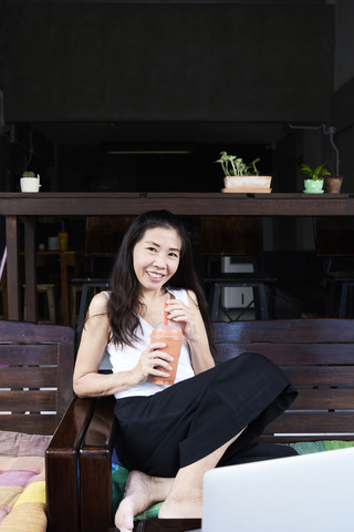 Portrait of smiling woman sitting on terrace bench drinking a smoothie stock photo