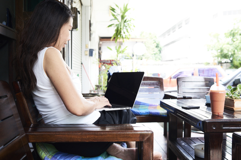 Frau mit Laptop auf einer Terrassenbank sitzend, lizenzfreies Stockfoto