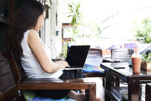 Woman using laptop sitting on terrace bench - IGGF00210