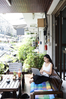 Woman using laptop sitting on terrace bench - IGGF00212
