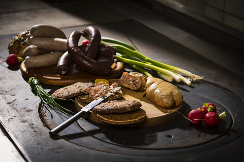 Liver sausage, blood sausage, spring onion, red radish, chives, mustard, bread on chopping board, hotplate stock photo