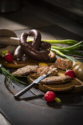 Liver sausage, blood sausage, spring onion, red radish, chives, mustard, bread on chopping board, hotplate - MAEF12460