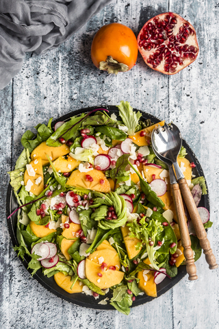 Kaki-Salat mit rotem Rettich, Granatapfel, Avocado und Käse, lizenzfreies Stockfoto