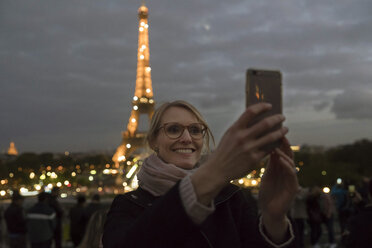 France, Paris, portrait of happy woman taking selfie with lighted Eiffel Tower in the background - CHPF00449