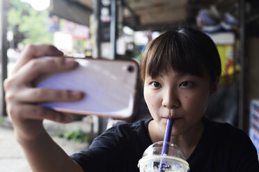 Porträt einer Frau, die einen Smoothie trinkt und dabei ein Selfie mit ihrem Smartphone macht - IGGF00222
