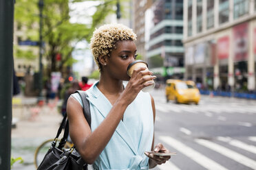 USA, New York, young blonde african-american woman with coffee mug and smart phone - MAUF01240