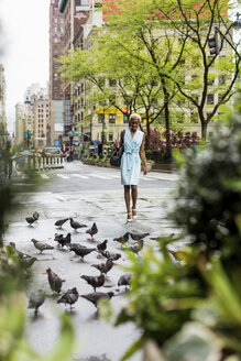 USA, New York, junge blonde afro-amerikanische Frau geht auf der Straße, Tauben - MAUF01242