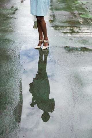 USA, New York, junge afroamerikanische Frau auf der Straße stehend, hohe Absätze, Wasserspiegelung in Pfütze, lizenzfreies Stockfoto