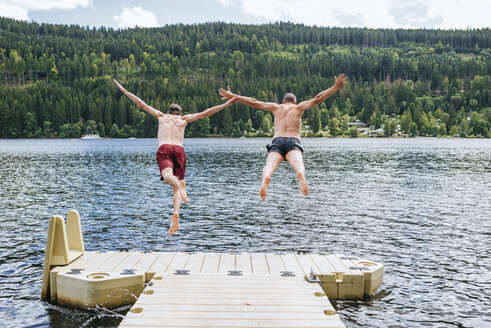Deutschland, Titisee, zwei Männer springen von einem Steg in den See - KIJF01717