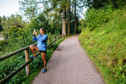 Germany, Triberg, Woman taking a photo with mobile phone on path - KIJF01721