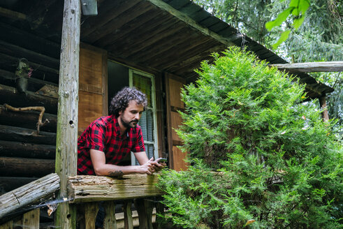 France, Strasbourg, man typing on mobile phone in old wooden hut - KIJF01731