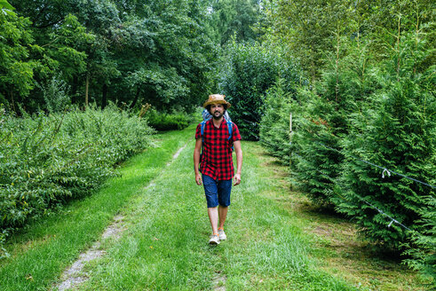 France, Strasbourg, man with travel backpack and straw hat walking on forest path - KIJF01733