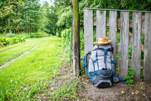 France, Strasbourg, travel backpack and straw hat in front of wooden fence on the way - KIJF01734