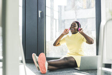 Happy businesswoman sitting on the floor listening to music - UUF12385