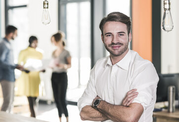 Portrait of smiling businessman in office with colleagues in background - UUF12387