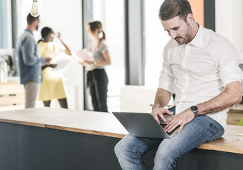 Geschäftsmann arbeitet am Laptop im Büro mit Kollegen im Hintergrund - UUF12388