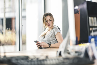 Geschäftsfrau mit Mobiltelefon am Schreibtisch im Büro - UUF12403