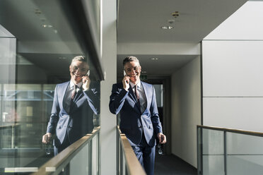 Lächelnder Geschäftsmann, der im Büro mit seinem Handy telefoniert - UUF12439