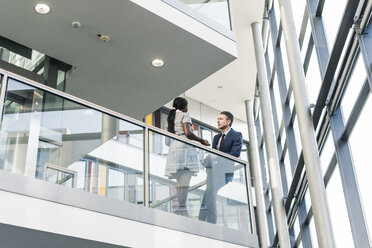 Businessman and woman talking on office floor - UUF12445