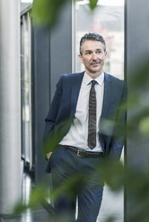 Businessman standing in office lobby - UUF12455