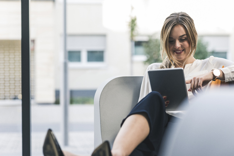 Smiling businesswoman sitting in lounge with tablet stock photo