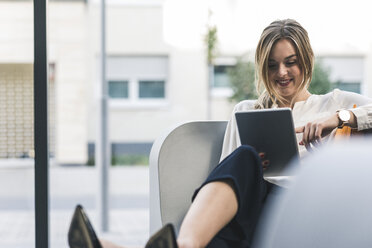 Smiling businesswoman sitting in lounge with tablet - UUF12458