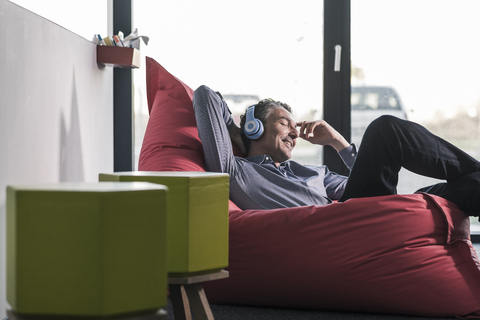 Lächelnder Geschäftsmann, der in einem Sitzsack sitzt und Kopfhörer trägt, lizenzfreies Stockfoto