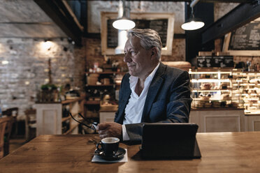 Älterer Geschäftsmann, der in einem Café sitzt, ein digitales Tablet benutzt und tagträumt - GUSF00181